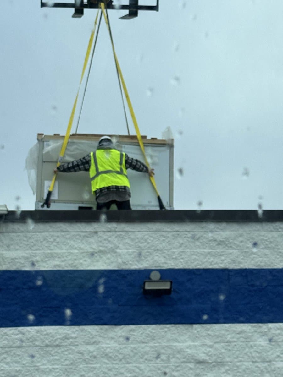 Technician in a safety harness rigging a rooftop unit with lifting slings