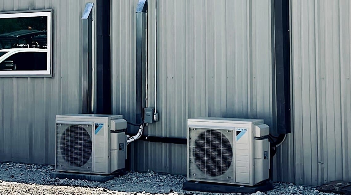 Pair of Daikin ductless condensers on gravel beside a metal building