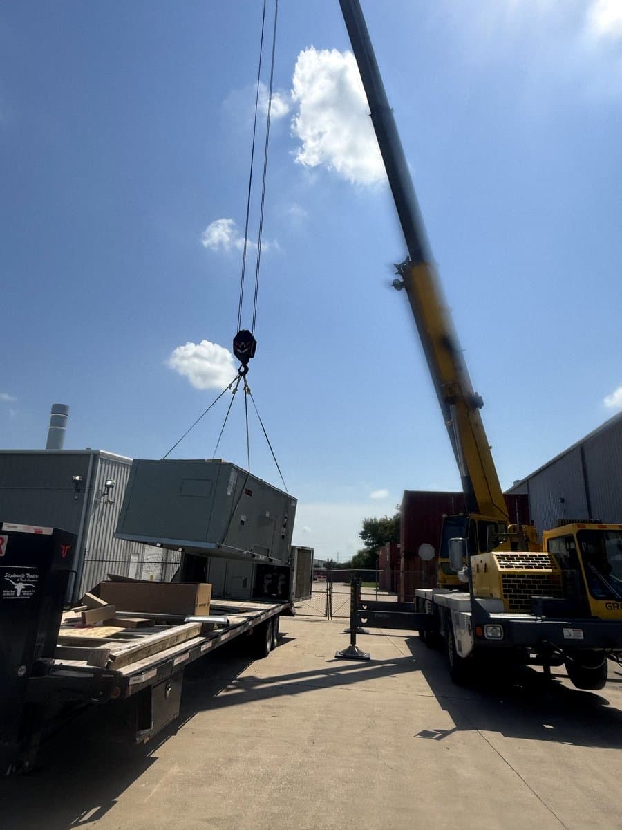 Crane truck staged alongside a building for a rooftop unit set
